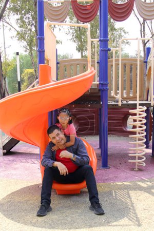 Divorced single dad plays with his brunette Latina daughter on the park slide enjoying quality time together celebrating Father's Day