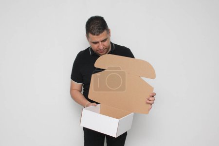 Latino adult man assembles a cardboard box following the instructions to achieve it