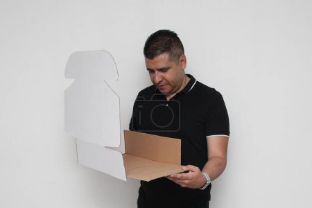 Hombre adulto latino ensambla una caja de cartón siguiendo las instrucciones para lograrlo