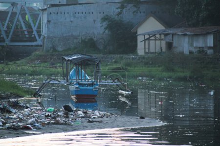 Traditionelles Boot in verschmutztem Fluss in der Nähe von Flussgebäuden festgemacht