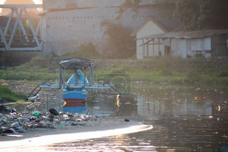 Bateau traditionnel mouillé dans une rivière polluée près de bâtiments riverains