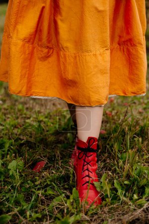 Téléchargez les photos : Vue rapprochée de la femme en jupe jaune et bottes rouges marchant sur l'herbe - en image libre de droit