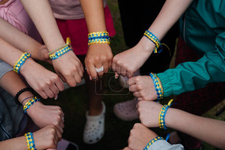Foto de Manos de un grupo de niños. La gente junta en las pulseras azules y amarillas de las cintas - el color de la bandera ucraniana. Amistad, unidad, apoyo. Espíritu de libertad y lucha. Gloria a Ucrania! - Imagen libre de derechos
