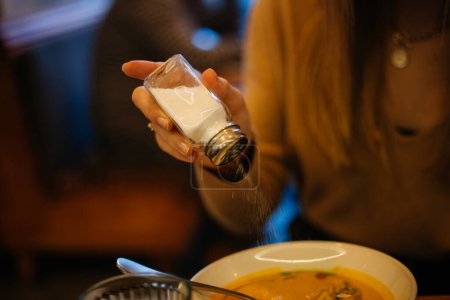 Foto de Chica sal sabrosa sopa de crema de calabaza con cuchara en un restaurante en un plato gourmet blanco sazonado con perejil cerca de vidrio borroso de agua - Imagen libre de derechos