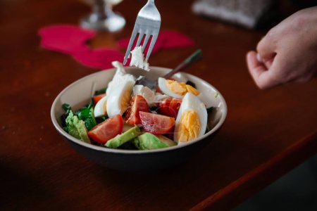 Téléchargez les photos : Un délicieux petit déjeuner frais et sain dans une assiette avec une fourchette. Tomates, avocats, œufs tordus - en image libre de droit