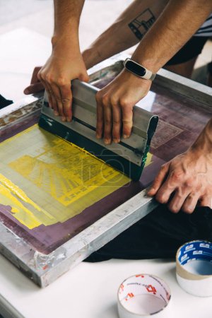 Foto de Trabajador masculino presionando tinta en el marco mientras usa la máquina de impresión en un taller - Imagen libre de derechos