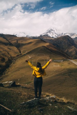 Photo for Rear view of a young woman looks on the Mount Kazbek and raising hands - Royalty Free Image