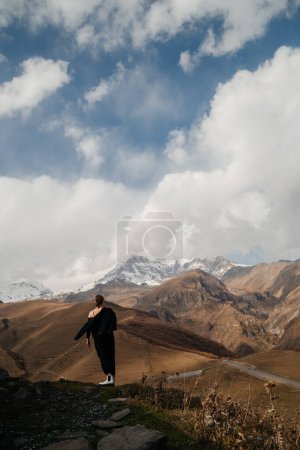 Téléchargez les photos : Belle jeune femme debout sur la colline et regarde sur les montagnes enneigées - en image libre de droit