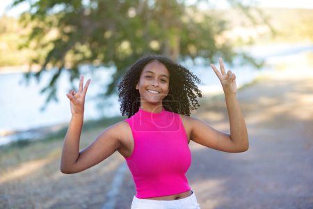 Téléchargez les photos : Winner girl passer une journée dans un parc faire le signe de la victoire avec ses doigts - en image libre de droit