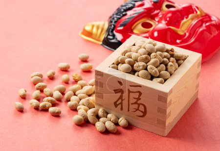 Foto de Beans for bean-throwing and masks of ogres placed on a background of red Japanese paper. Japanese ogres. Setsubun image. - Imagen libre de derechos
