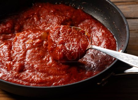 Téléchargez les photos : Ramassez la sauce tomate dans la casserole avec une cuillère. Scène de cuisine. Gros plan. Fond en bois. - en image libre de droit