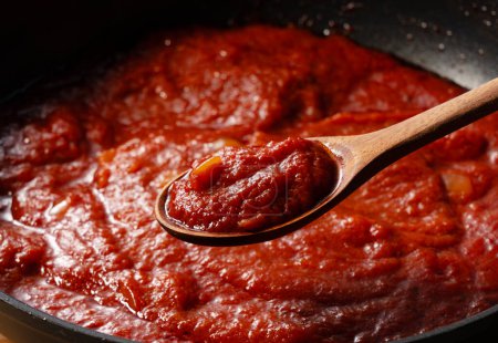 Téléchargez les photos : Ramassez la sauce tomate dans la casserole avec une cuillère. Scène de cuisine. Gros plan. Fond en bois. - en image libre de droit