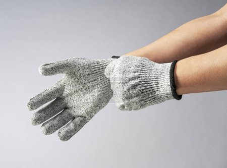 Téléchargez les photos : Main masculine portant des gants résistant au couteau sur fond gris. - en image libre de droit