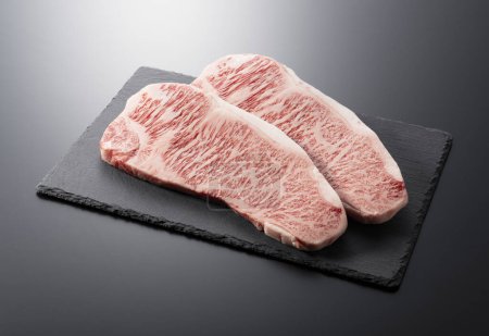 Fresh raw beef steak placed on a stone plate against a black background. Wagyu beef steak.