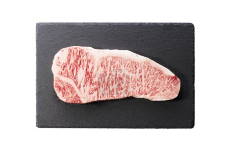 Fresh raw beef steak placed on a stone plate against a white background. Wagyu beef steak. View from directly above.