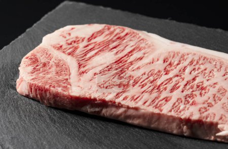 Fresh raw beef steak placed on a stone plate against a black background. Wagyu beef steak.