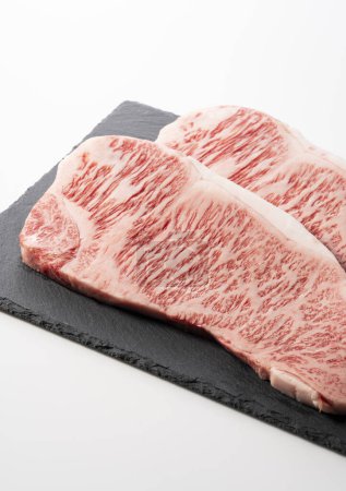Fresh raw beef steak placed on a stone plate against a white background. Wagyu beef steak.