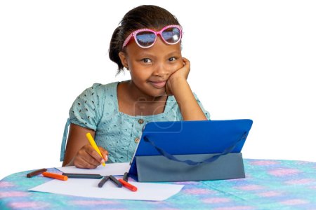 Téléchargez les photos : Portrait of Little African girl doing schoolwork at desk with digital tablet. Isolated on a white background. - en image libre de droit