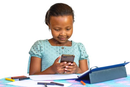 Téléchargez les photos : Portrait of Little African girl doing homework at desk with digital tablet and smartphone. Isolated on a white background. - en image libre de droit