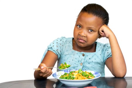 Portrait of Little African kid sitting at dinner table with a negative facial expression. Isolated on white background.