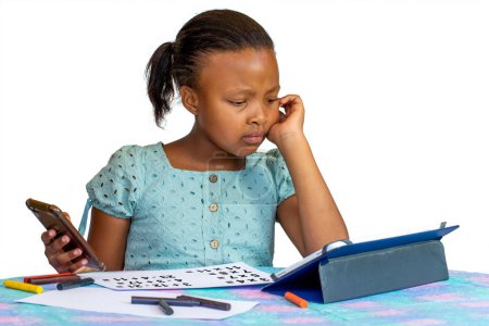 Téléchargez les photos : Portrait of Little African girl doing maths homework at desk with digital tablet and smartphone. Isolated on a white background. - en image libre de droit