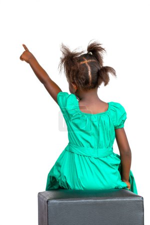 Photo for Rear view of little African girl in green dress pointing with finger. Isolated on white background. - Royalty Free Image