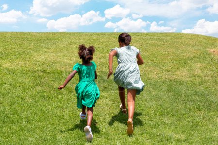 Téléchargez les photos : Full-length action portrait of two young African girls running in grass field against a blue sky. - en image libre de droit