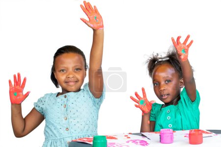 Photo for Two African girls having fun with color paint at the table.  Isolated against a white background. - Royalty Free Image