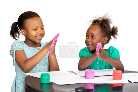 Photo for Two African girls getting creative with color paint at the table.  Isolated against a white background. - Royalty Free Image