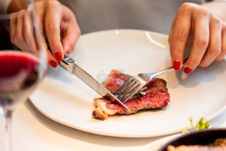 Photo for Close up detail of female hands cutting sirloin steak in gourmet restaurant. - Royalty Free Image