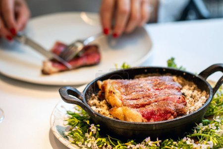 Foto de Primer plano de filete de solomillo wagyu medio raro en tazón de hierro con mujer comiendo en el fondo. - Imagen libre de derechos