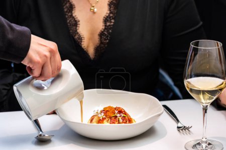 Téléchargez les photos : Détail rapproché de la femme dînant dans un restaurant gastronomique. Serveuse versant de la soupe de fruits de mer avec du homard près d'un verre de vin blanc. - en image libre de droit