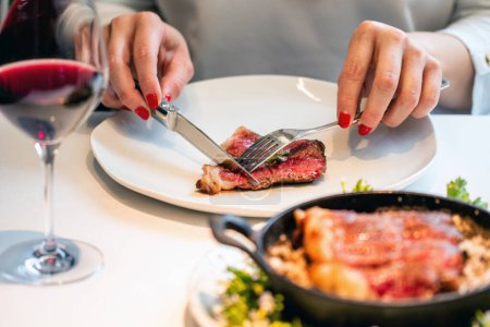 Photo for Close up of Woman enjoying medium done sirloin steak in restaurant. Female hands cutting meat on plate. - Royalty Free Image