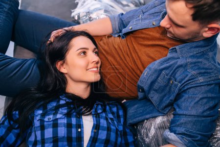 Téléchargez les photos : Amour jeune couple regarder l'autre étreinte et de détente sur le canapé à la maison - en image libre de droit