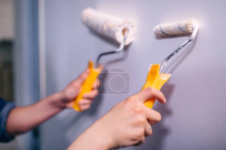 Foto de Primer plano de las manos utilizando rodillos de espuma que aplican pintura blanca a las paredes. - Imagen libre de derechos
