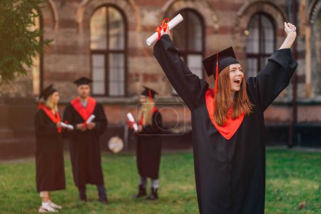 Foto de Estudiante sonriente en traje académico y gorra de graduación con un diploma, gritando de felicidad, habiendo recibido un diploma de graduación de la universidad. - Imagen libre de derechos