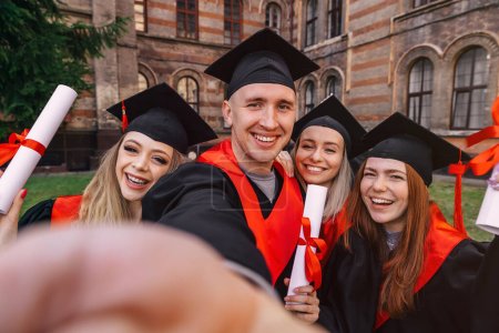 Foto de Grupo feliz graduados estudiantes utilizan el teléfono móvil para tomar selfie juntos. Después de recibir los diplomas. - Imagen libre de derechos