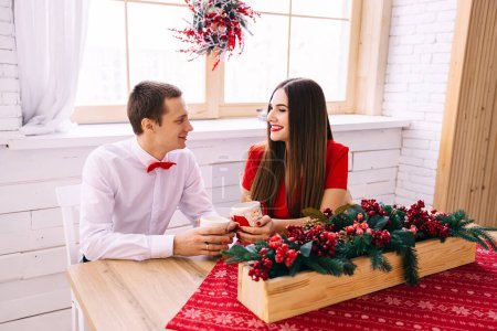 Foto de Mujer y hombre sentados a la mesa bebiendo bebida caliente. sobre la mesa y ventana Decoraciones navideñas. - Imagen libre de derechos
