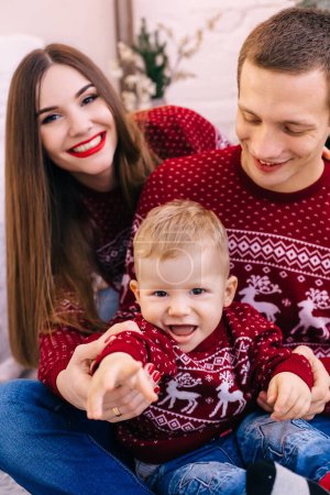 Photo for Closeup of mom, dad and little son near Christmas tree. boy holding a big box with a gift. family look. - Royalty Free Image