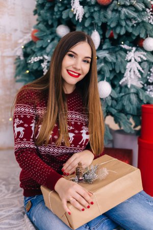 Foto de Retrato de mujer en suéter con regalo en el fondo del árbol de Navidad. - Imagen libre de derechos
