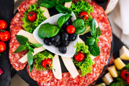 Téléchargez les photos : Vue de dessus sur l'assiette avec salami, fromage et olives dans l'assiette centrale. laitue et basilic pour un beau plat. mariage - en image libre de droit