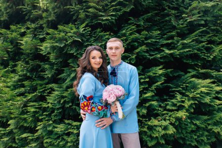 Téléchargez les photos : Un couple élégant de jeunes mariés heureux se promènent dans le parc le jour de leur mariage avec un bouquet de fleurs - en image libre de droit