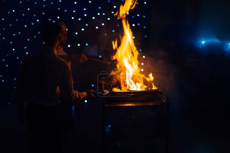 Photo for Lviv, Ukraine - 5 November 2017 - Chef cooks meat in front of guests. Fire presentation at wedding reception. - Royalty Free Image