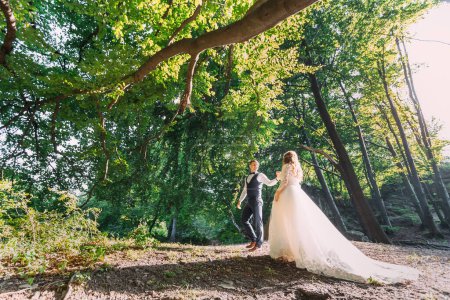 Foto de El novio toma la mano de la novia y caminan por el bosque. hermosa naturaleza. - Imagen libre de derechos
