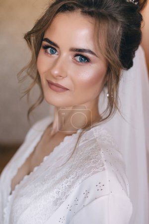 Téléchargez les photos : Gros plan portrait de mariée dans un peignoir blanc avec maquillage délicat et cheveux, derniers préparatifs pour la cérémonie. - en image libre de droit