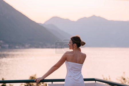 Foto de Hermosa joven modelo en bata de pie en Balcón vista en la orilla del mar Kotor, Montenegro. - Imagen libre de derechos