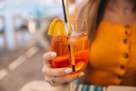 Photo for Young girl in a restaurant holding a cocktail aperol spritz in a glass - Royalty Free Image