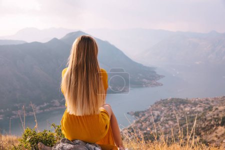 Photo for Rear view of young woman in yellow dress, who looking from above to the Kotor city and Boka bay, Montenegro. - Royalty Free Image