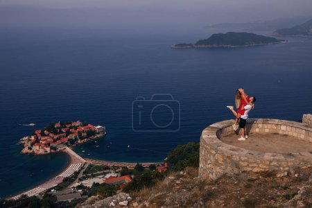 Foto de Romántica pareja joven enamorada sobre la orilla del mar sobre la isla de Sveti Stefan en Budva, Montenegro. Viajar. Vacaciones. Familia
. - Imagen libre de derechos