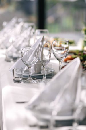 Téléchargez les photos : Table à une réception de mariage de luxe. Servir la vaisselle, verres en verre, serveurs de travail - en image libre de droit
